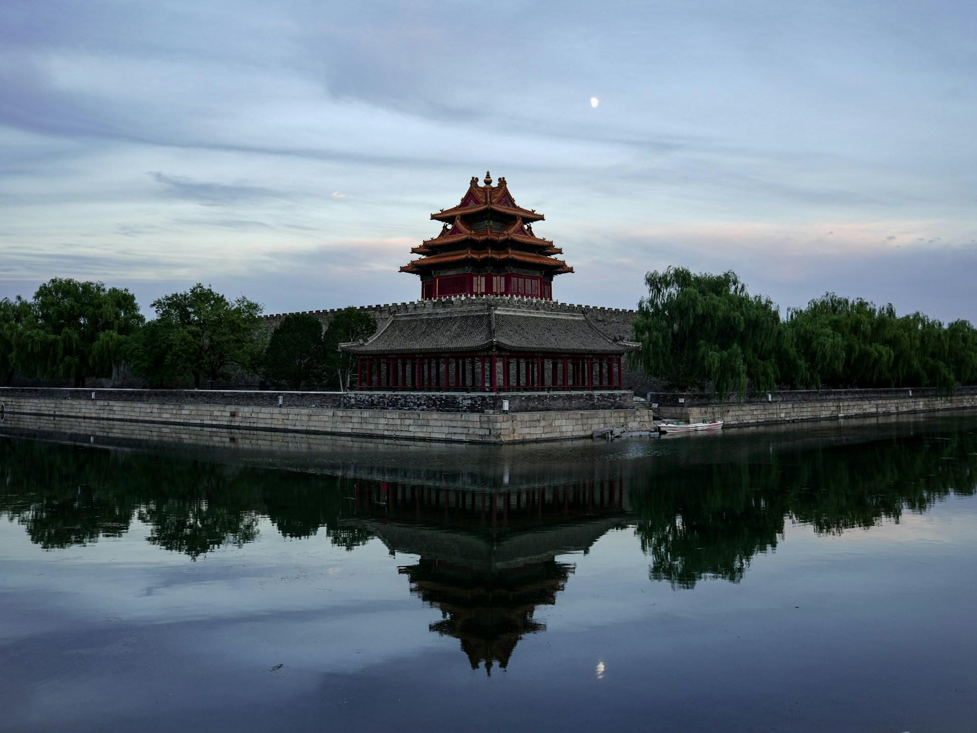 A corner watchtower of the Forbidden City reflected in the moat at dusk