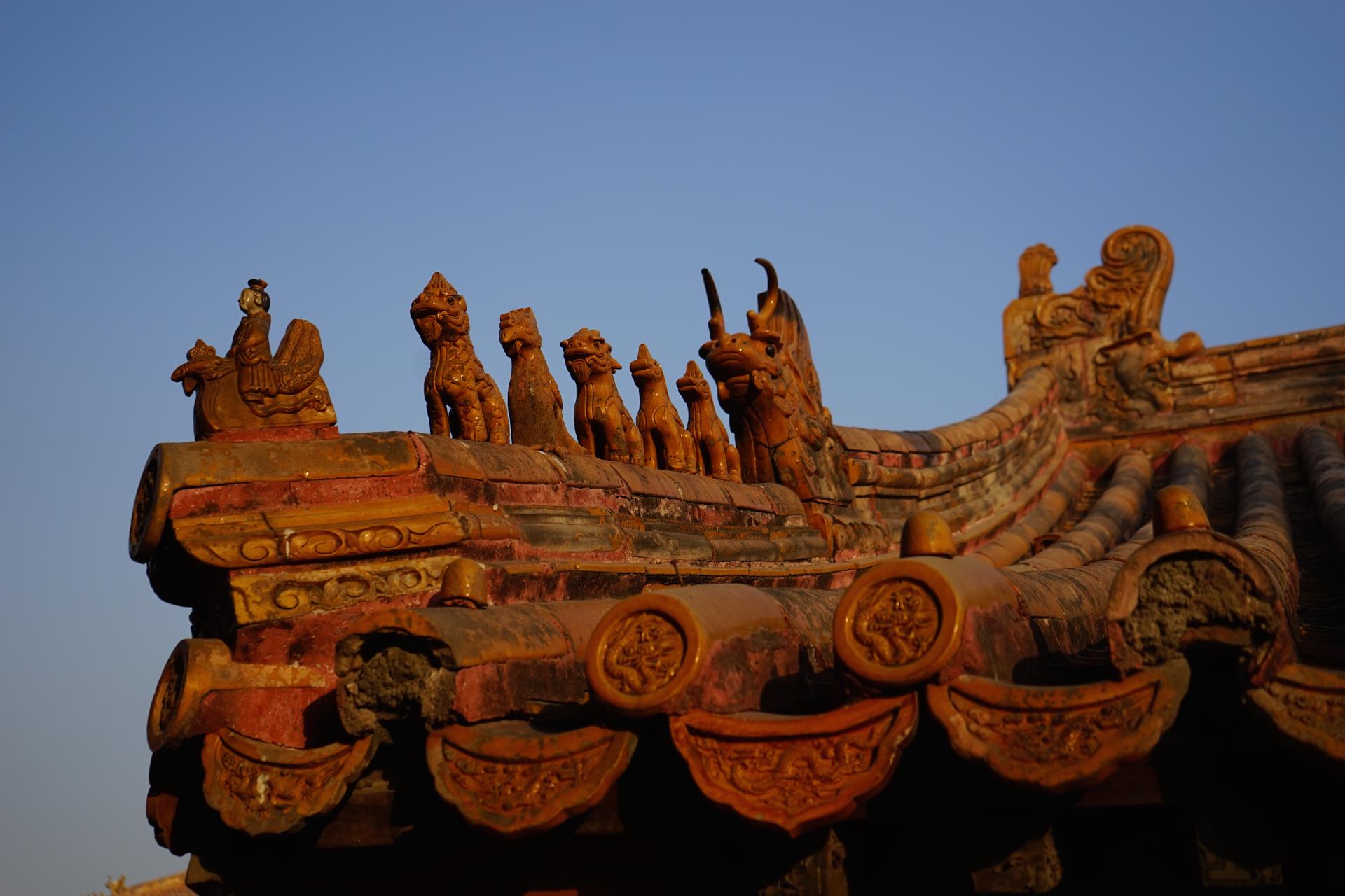 A procession of glazed guardian beasts marching along a golden imperial roof ridge