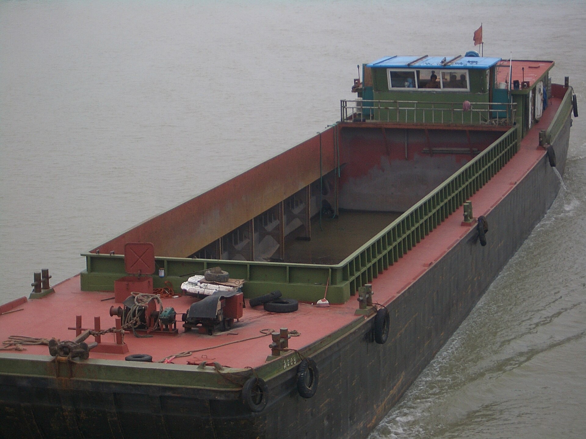 A rust-decked empty-hold cargo barge with its wheelhouse in use, hauling freight on the Grand Canal near Yangzhou