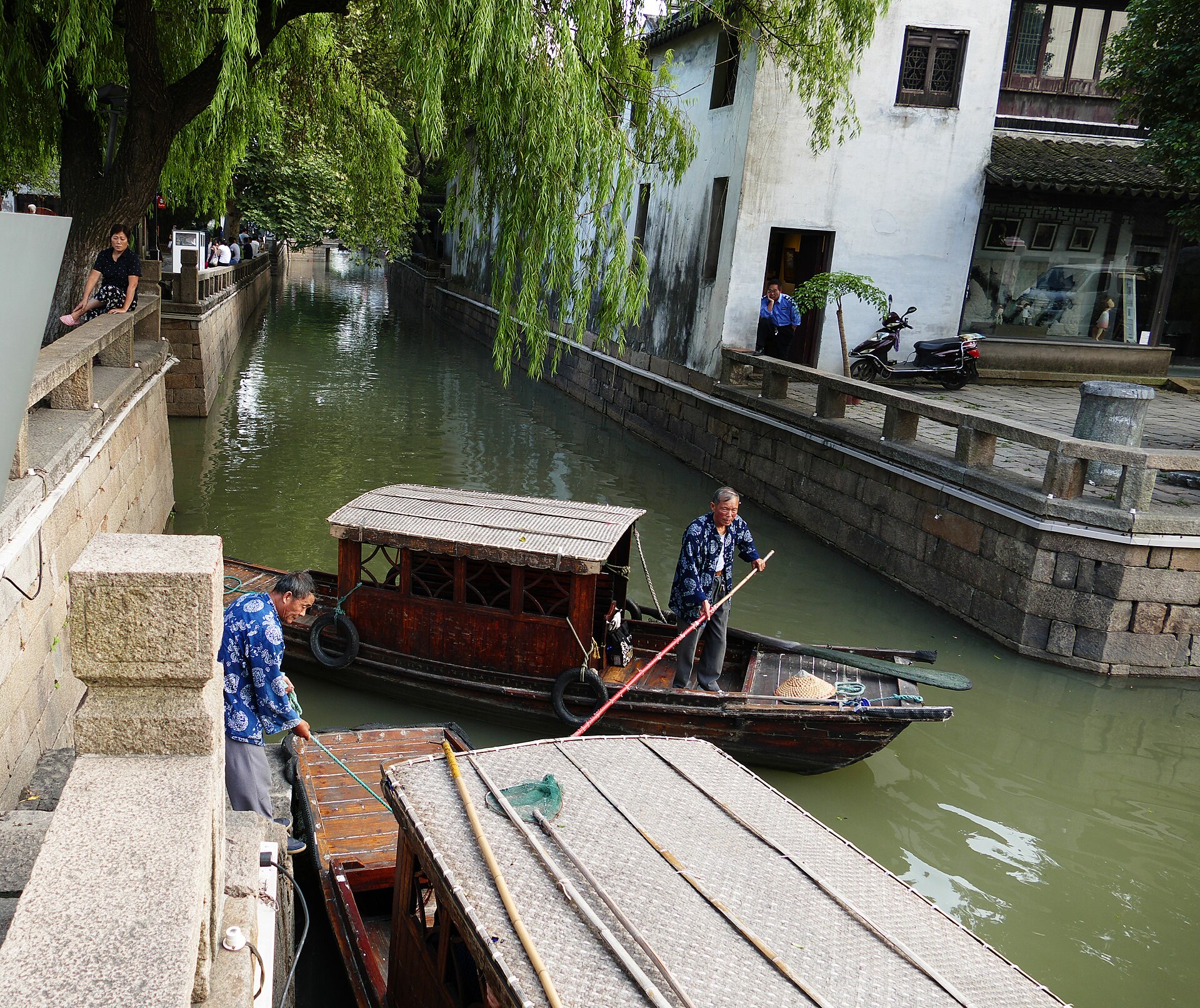Two boatwomen poling wooden sculling boats down the narrow willow-hung canal beside Pingjiang Road, Suzhou