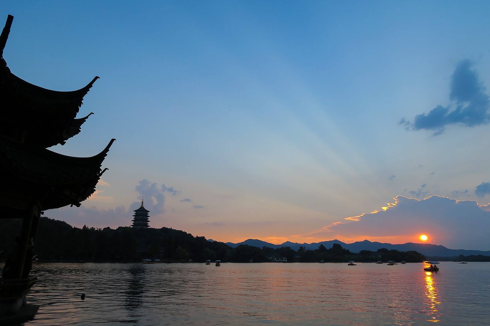 Sunset over West Lake with a lakeside pavilion silhouette, the Leifeng Pagoda and small boats on the water
