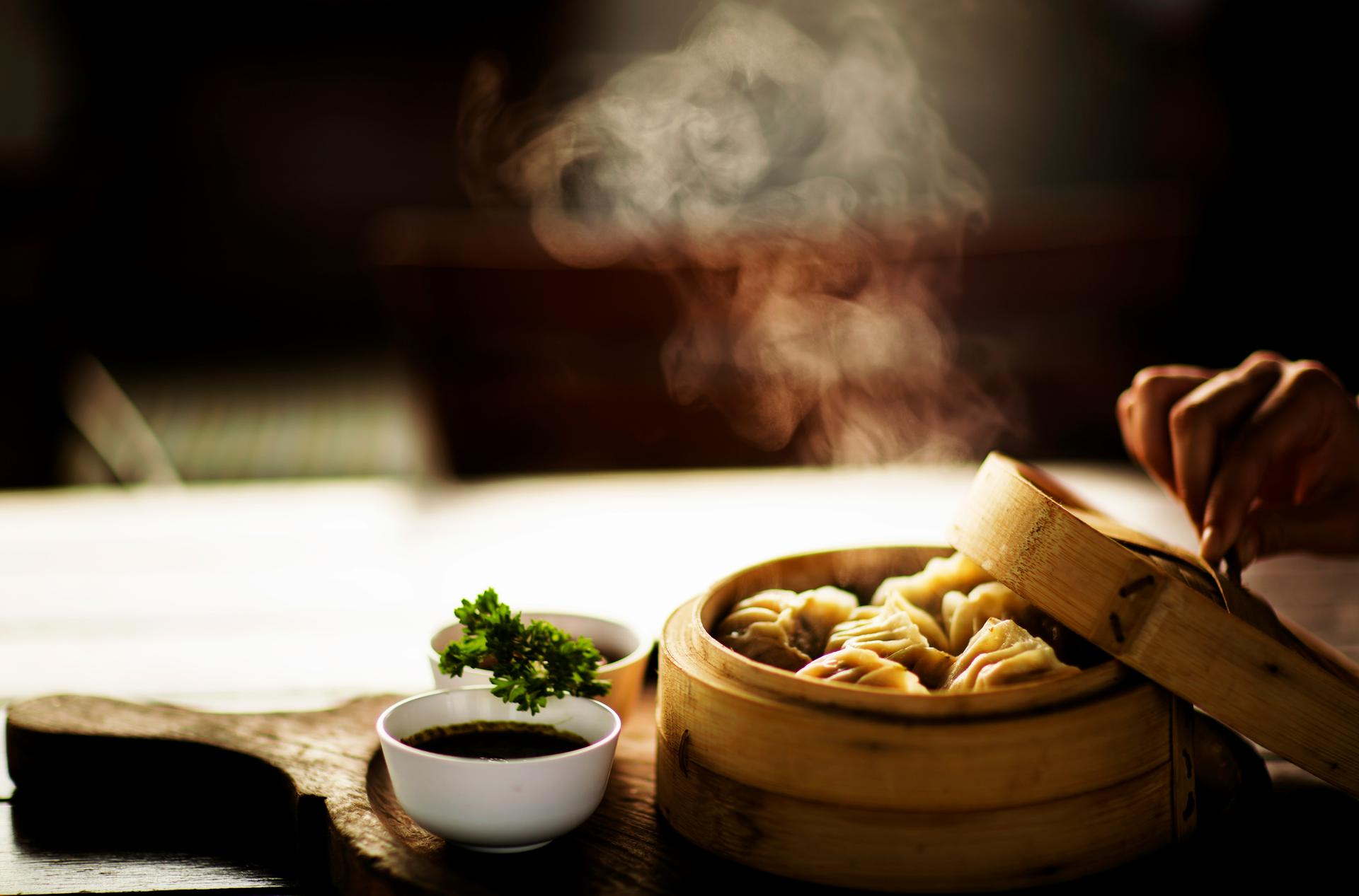 Steam rising from a bamboo steamer of dim sum as the lid is lifted