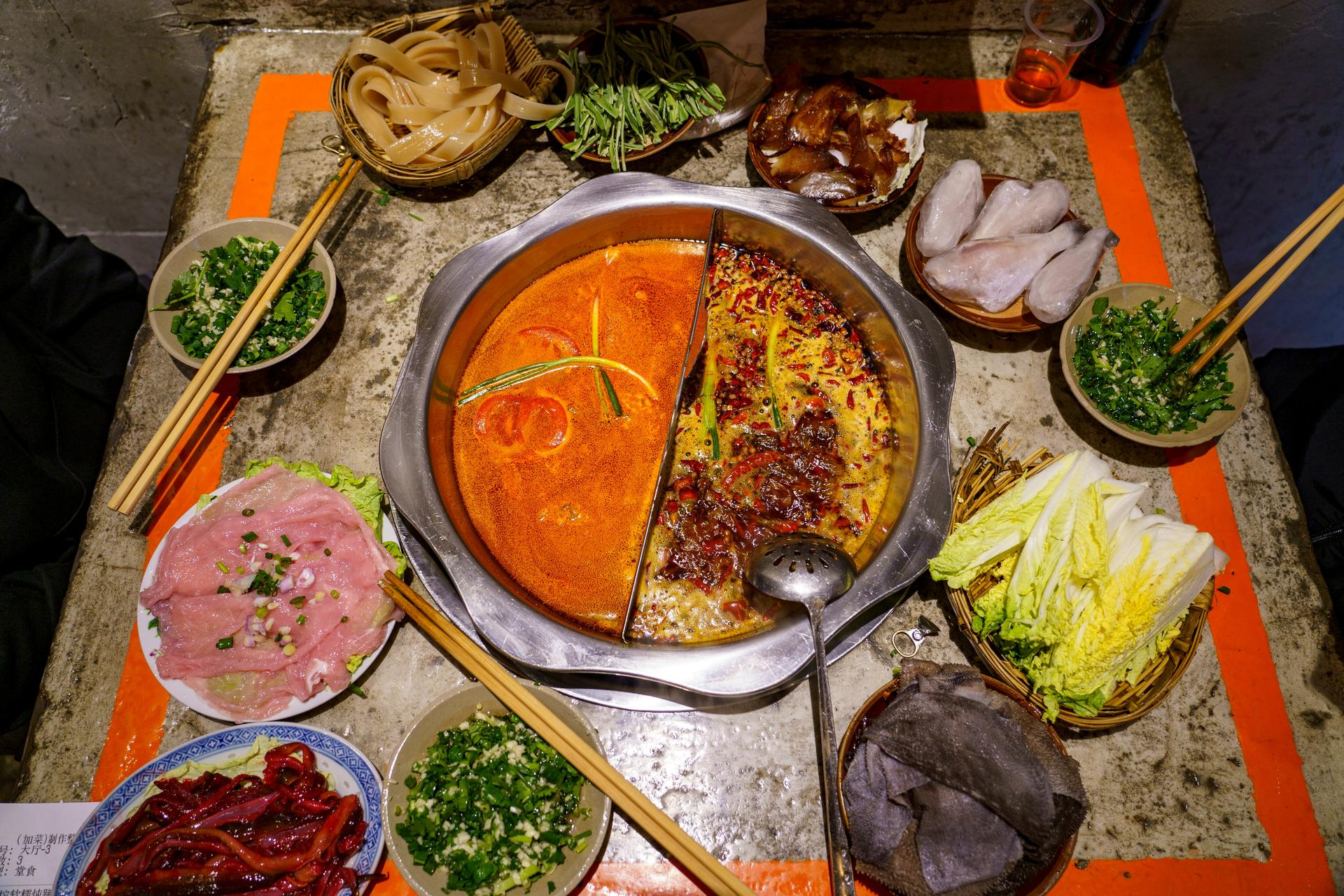 A yin-yang Sichuan hotpot surrounded by plates of raw ingredients