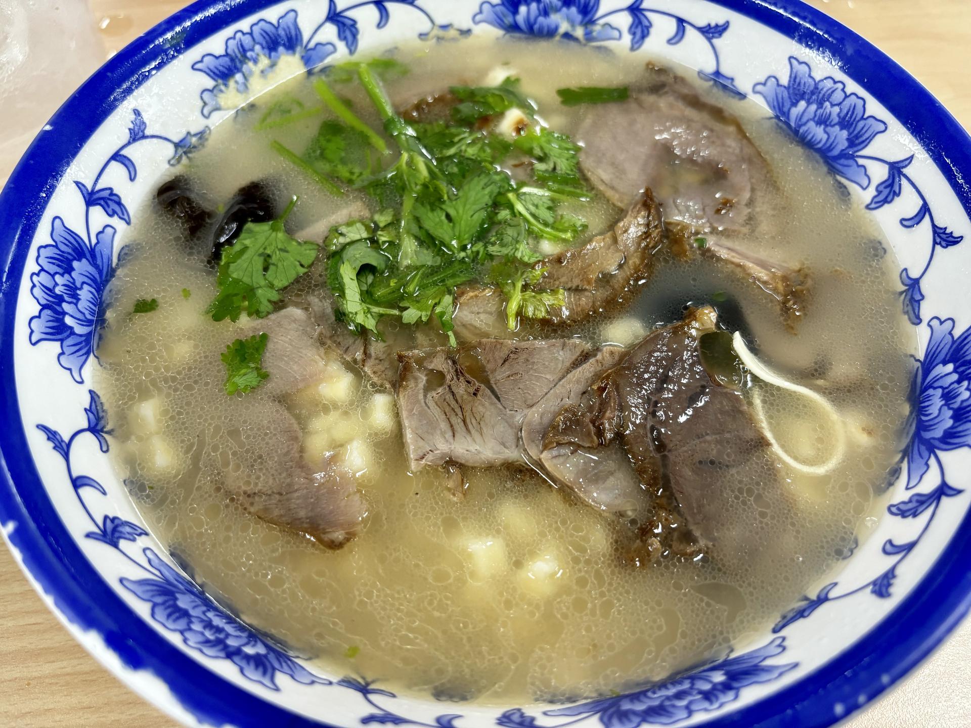 A bowl of Xi'an beef paomo with hand-torn bread and coriander