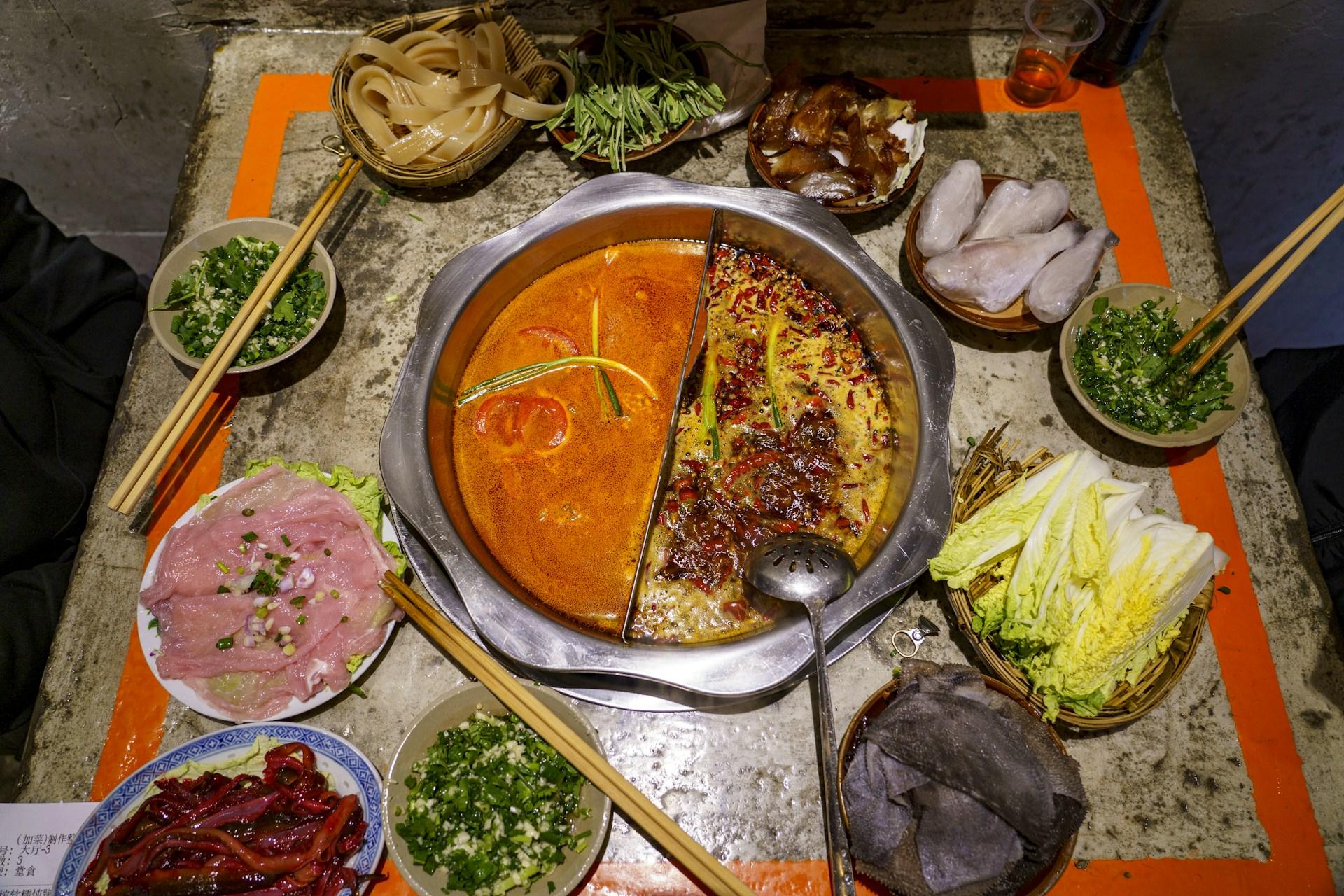 A divided hotpot — mild broth on one side, chilli-red on the other — surrounded by raw dishes