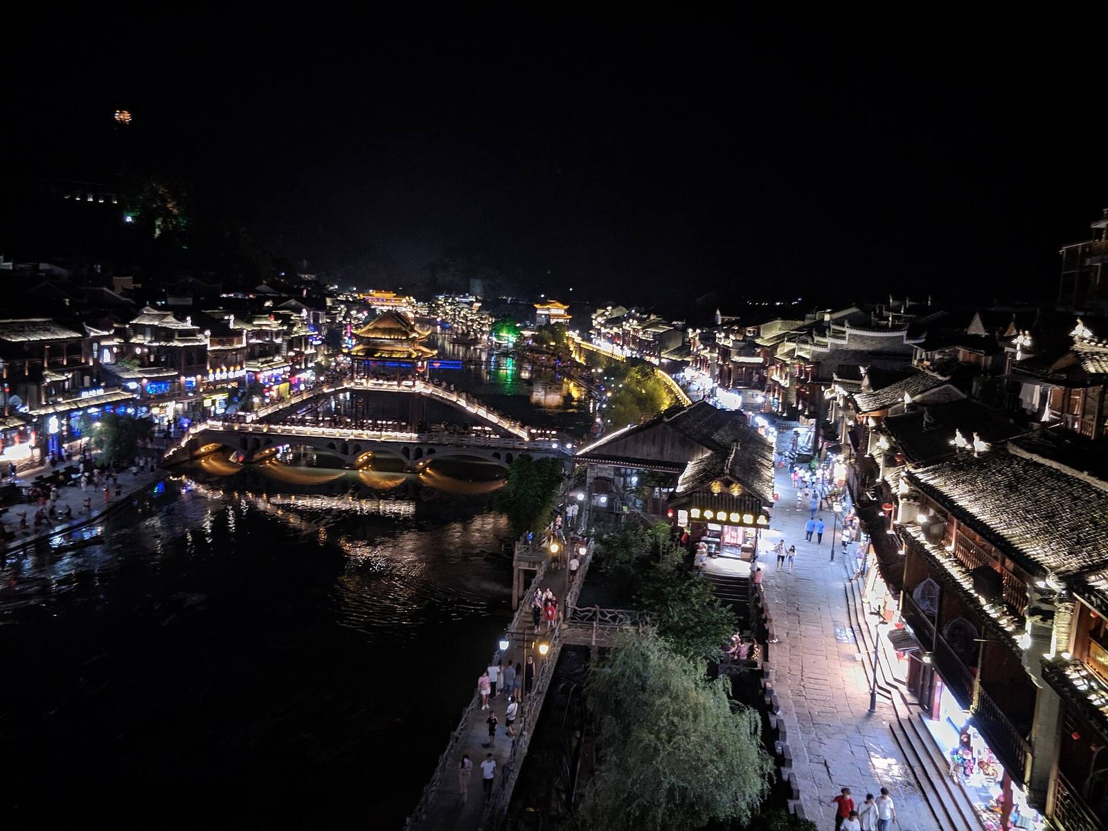 Fenghuang old town at night, its covered bridge and stilted riverside houses lit above the Tuo River
