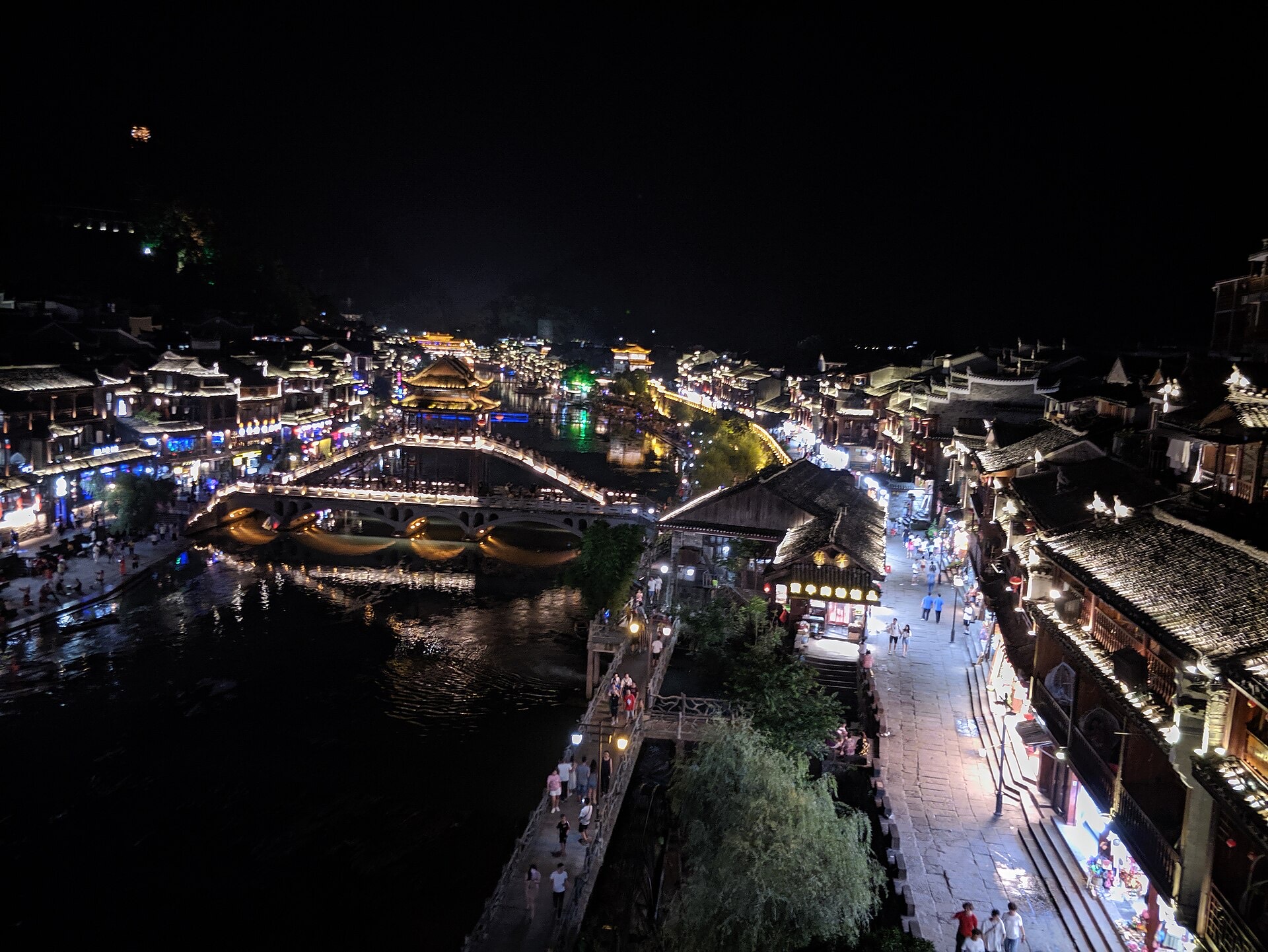 Fenghuang old town at night, its covered bridge and stilted riverside houses lit above the Tuo River