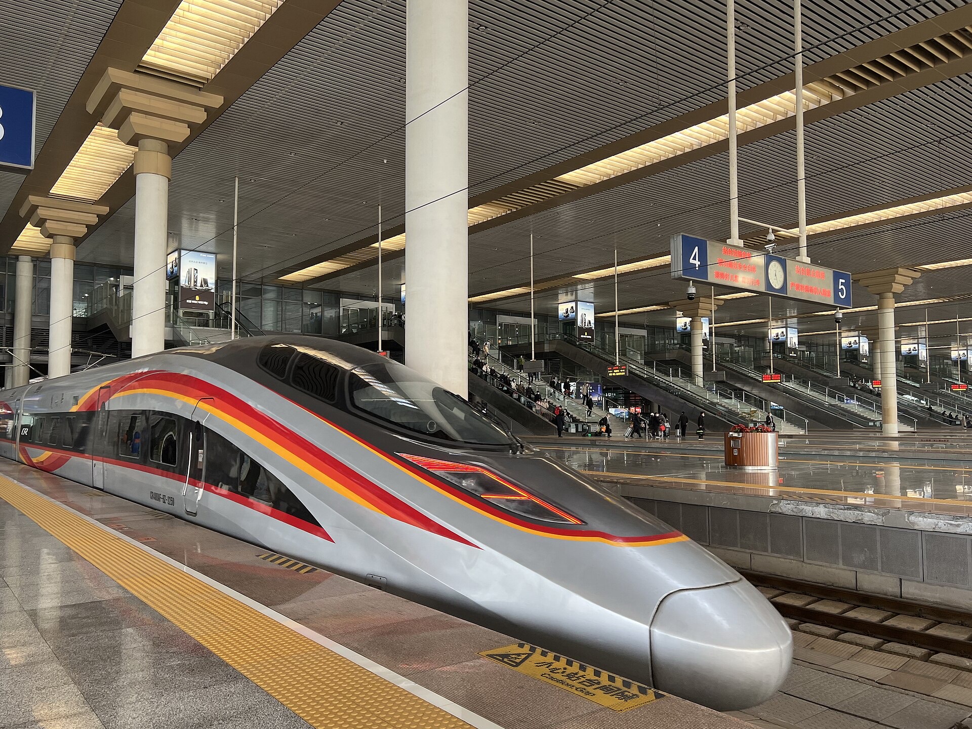 A Fuxing bullet train in red and gold ribbon livery boarding at a platform of Nanjing South station