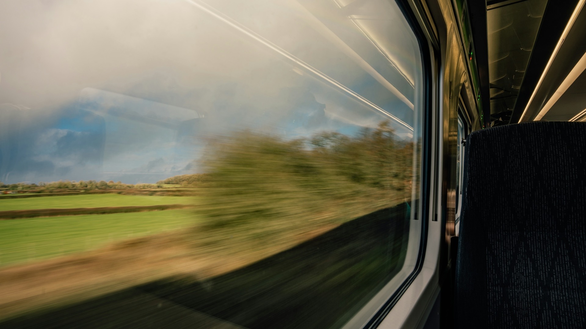 Green countryside blurring past the window of a fast-moving train, with the carriage interior softly dark