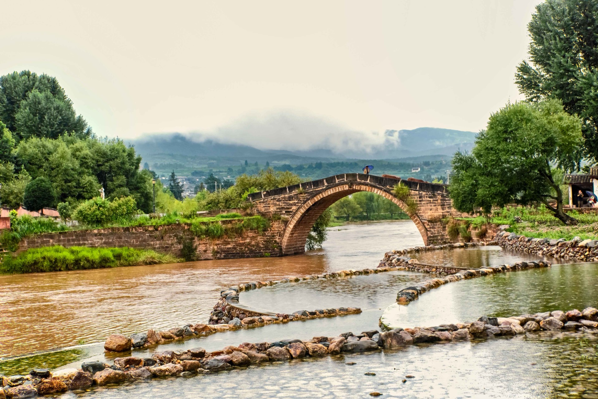 The old stone Yujin Bridge over the Heihui river at Shaxi, under mountain cloud